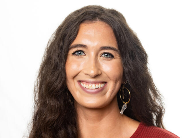 Emma Altomonte, a woman with long, curly hair, a red top and hoop earrings.